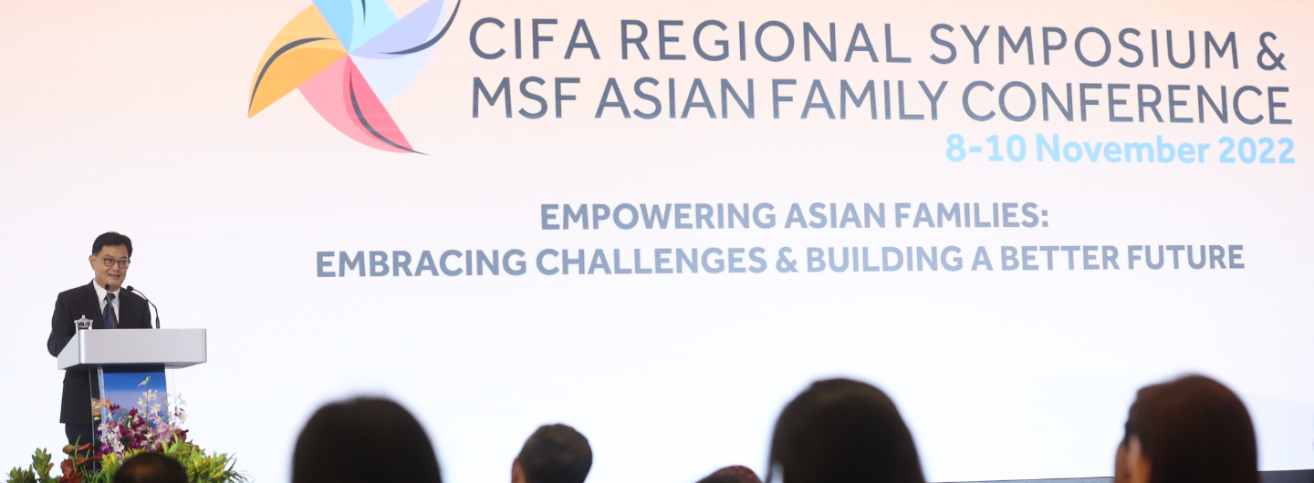 Man in suit at podium, "CIFA REGIONAL SYMPOSIUM" backdrop, audience visible.
